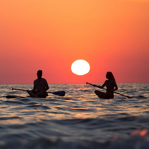 Ein Paar auf Surfbrettern mit Paddeln vor einem Sonnenuntergang