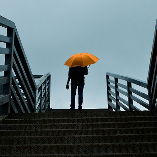 Mensch mit einem orangefarbenen Schirm, der eine Treppe hinaufsteigt
